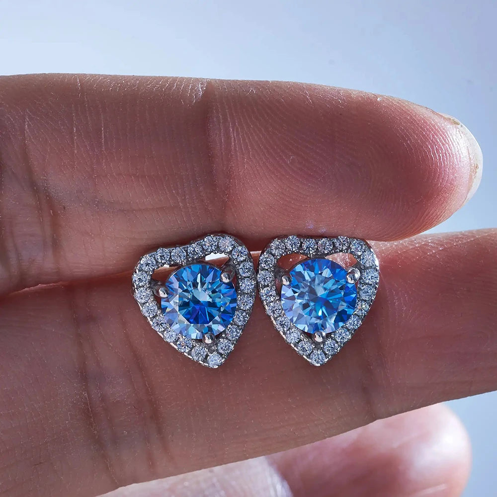 Moissanite Heart Halo Stud Earrings in Sterling Silver — Blue heart halo studs held in hand — BandsCo Straps