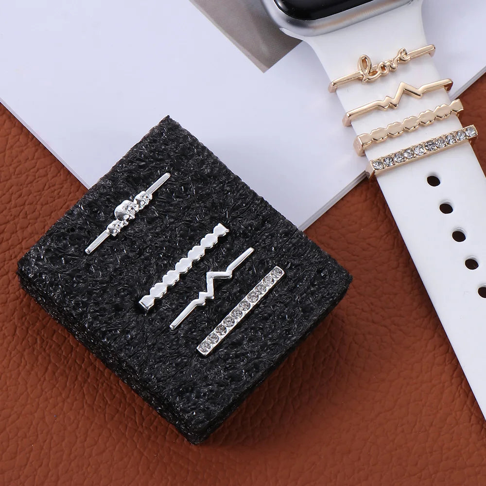 Decorative metal charms for Apple Watch bands, featuring silver and gold designs on a textured background.