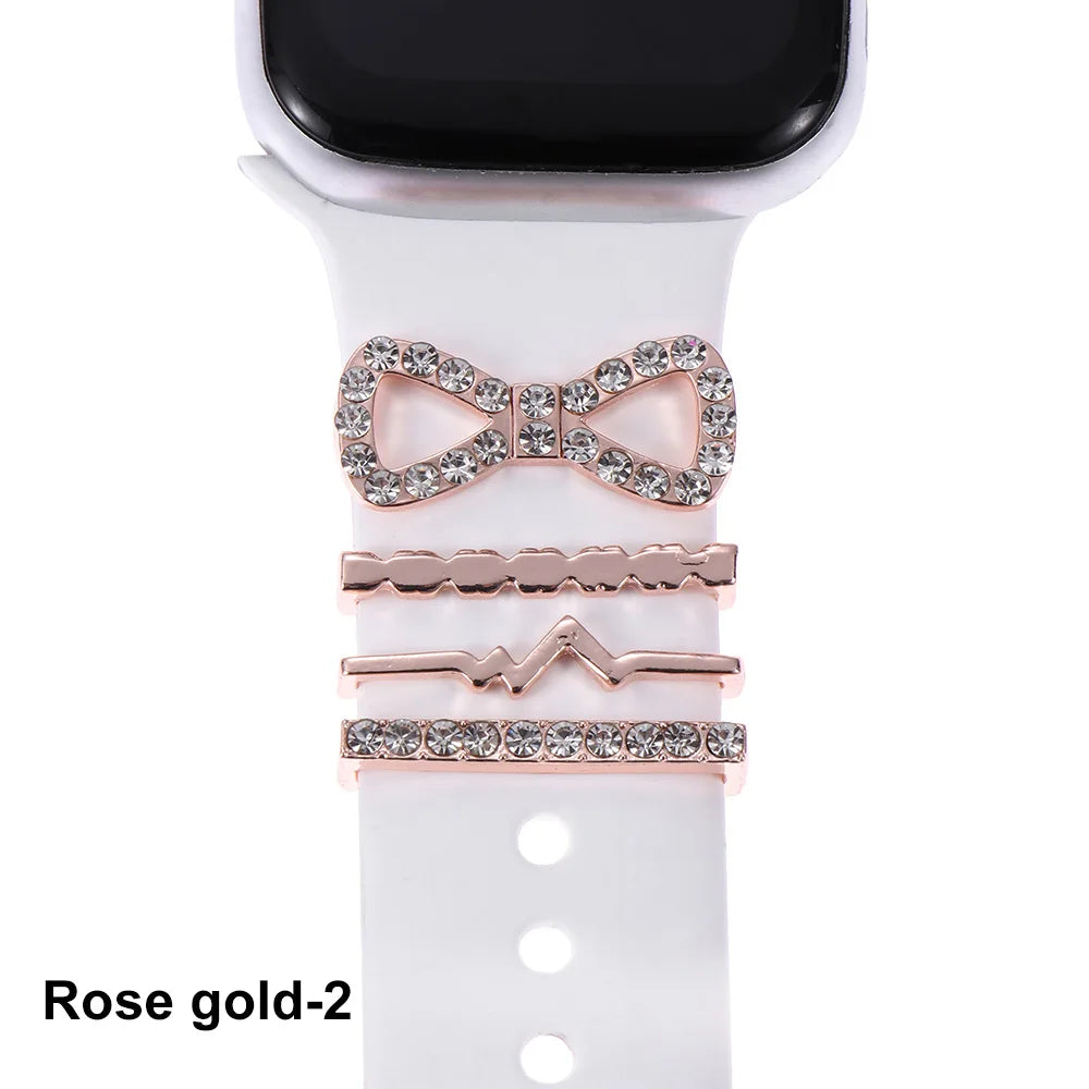 Decorative rose gold metal charms on white Apple Watch band, including a bow and stylish patterns.