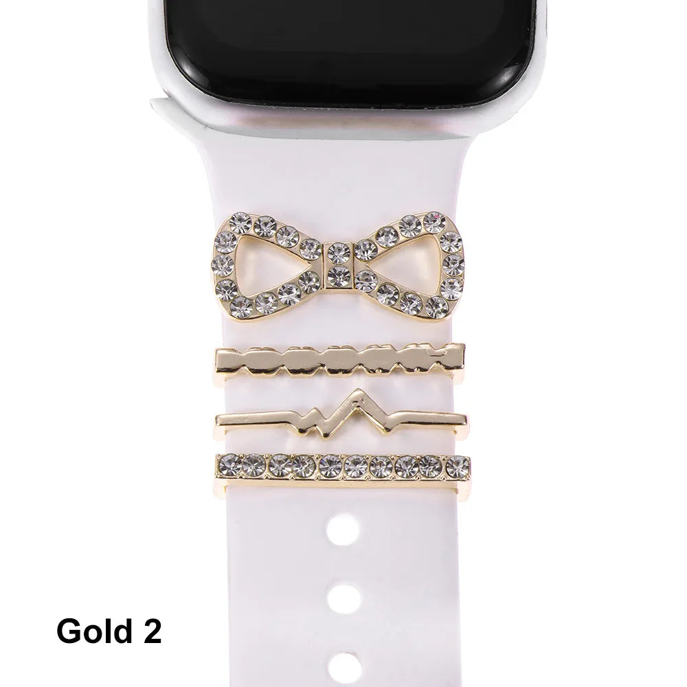 Decorative gold metal charms on a white Apple Watch band, featuring a bow and stylish accents for elegance.