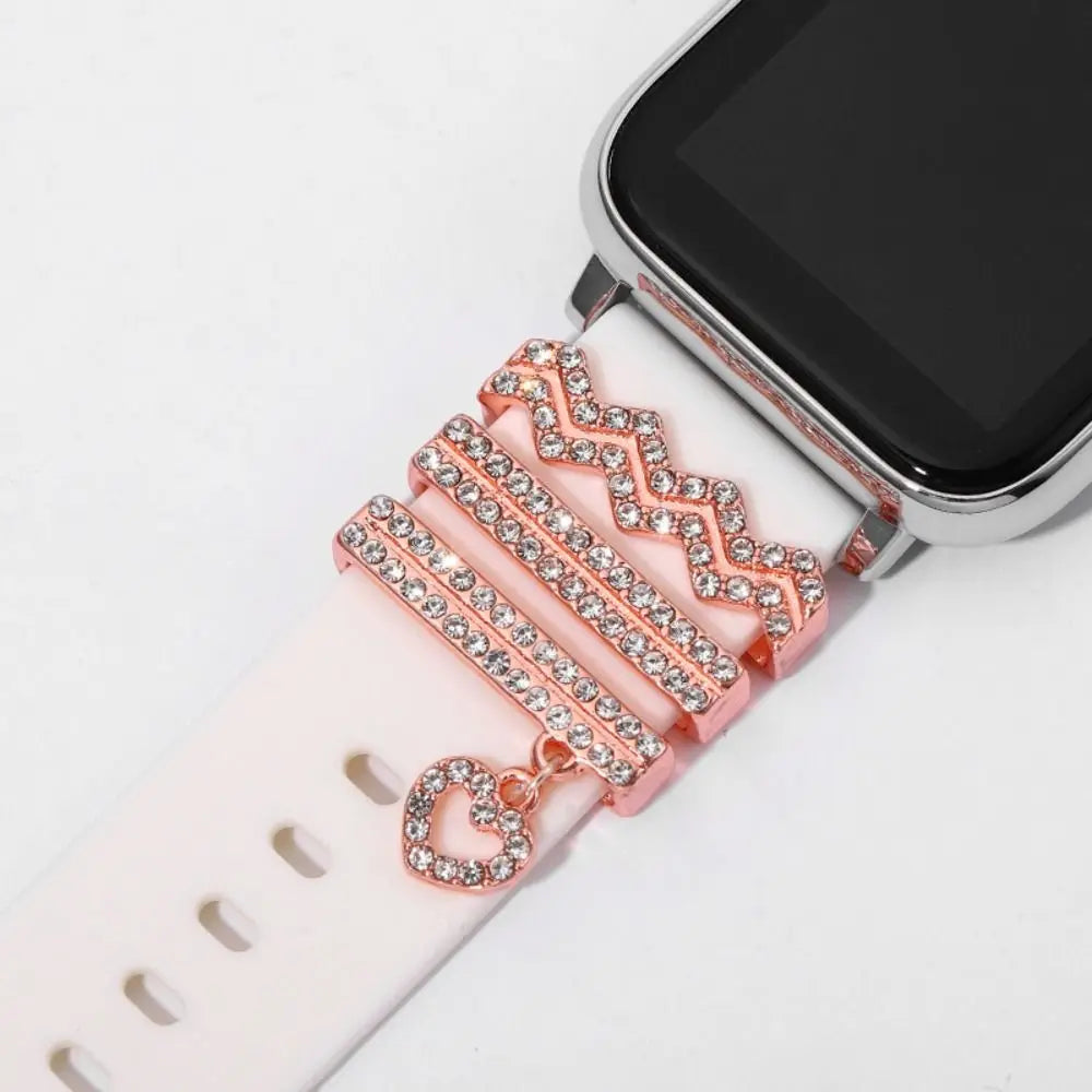 Decorative metal charms on a pink Apple Watch band, featuring rhinestones and a heart charm for stylish enhancement.