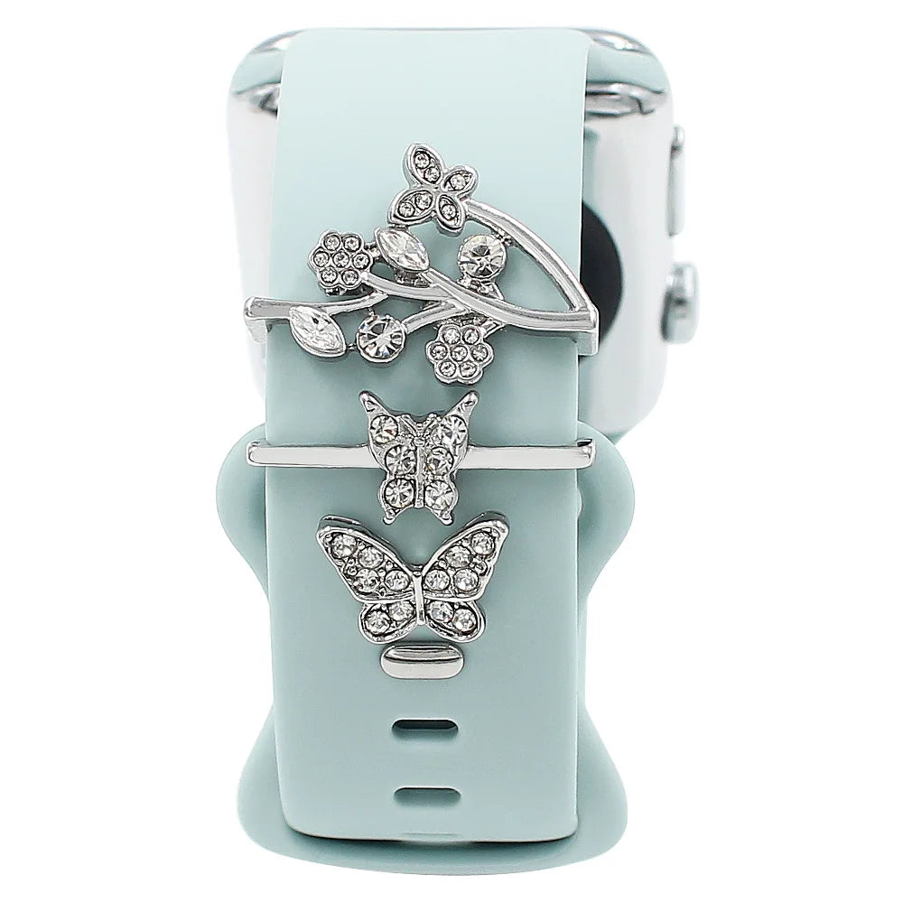 Decorative metal charms on light blue Apple Watch band, featuring butterfly and floral designs for stylish elegance.
