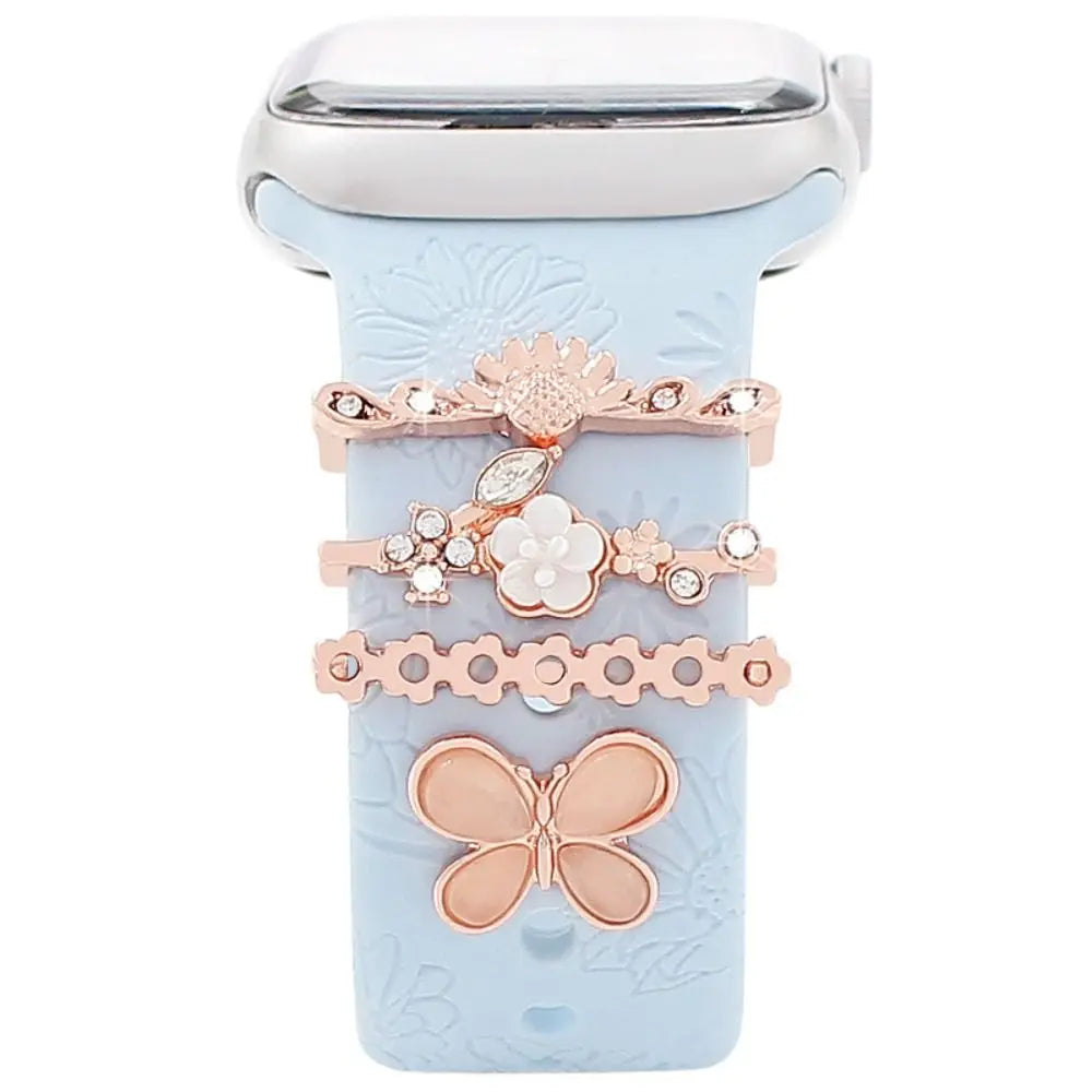 Decorative metal charms on a light blue Apple Watch band, featuring floral and butterfly designs for added style.