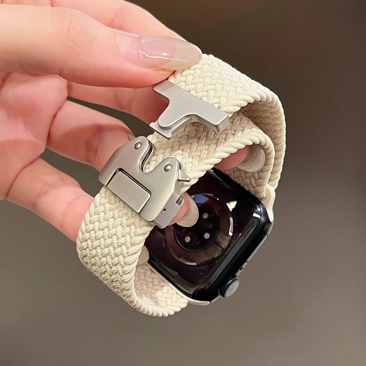 Ivory braided Apple Watch band with open buckle held in hand