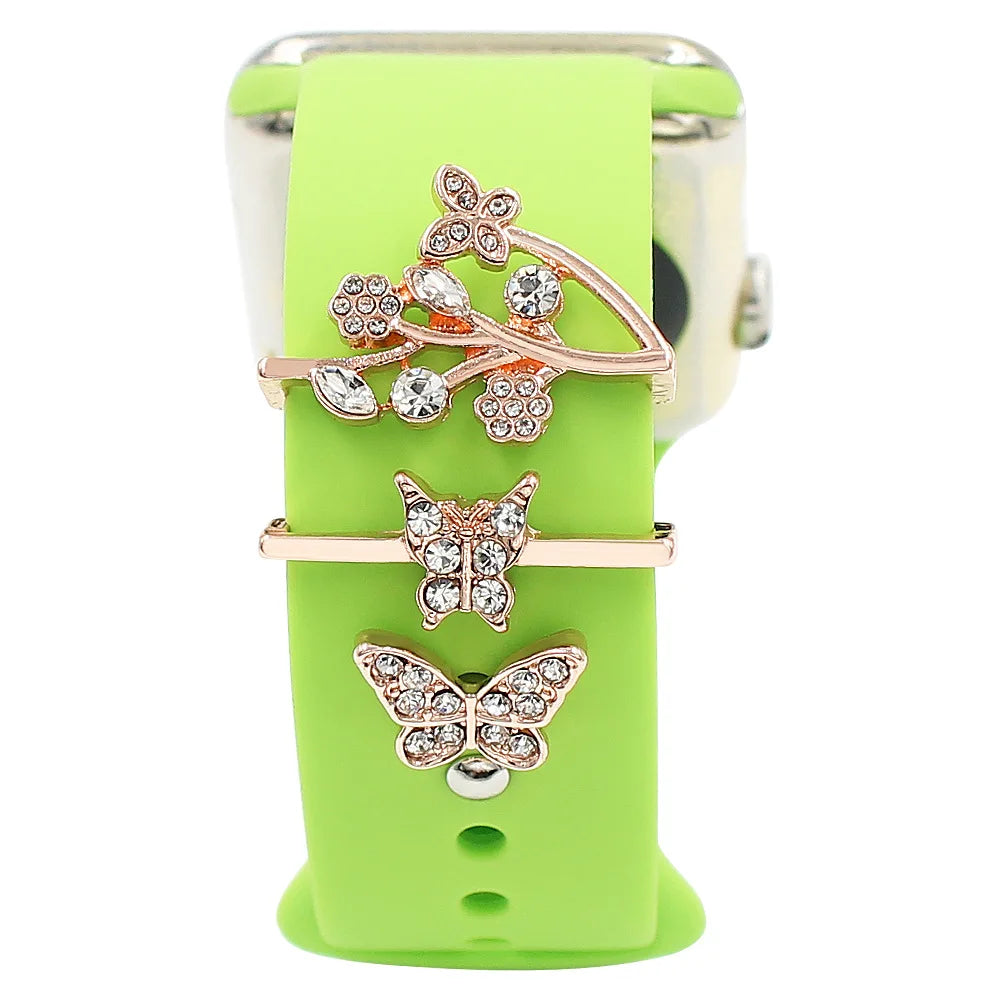 Decorative metal charms featuring butterflies and floral designs on a green Apple Watch band.