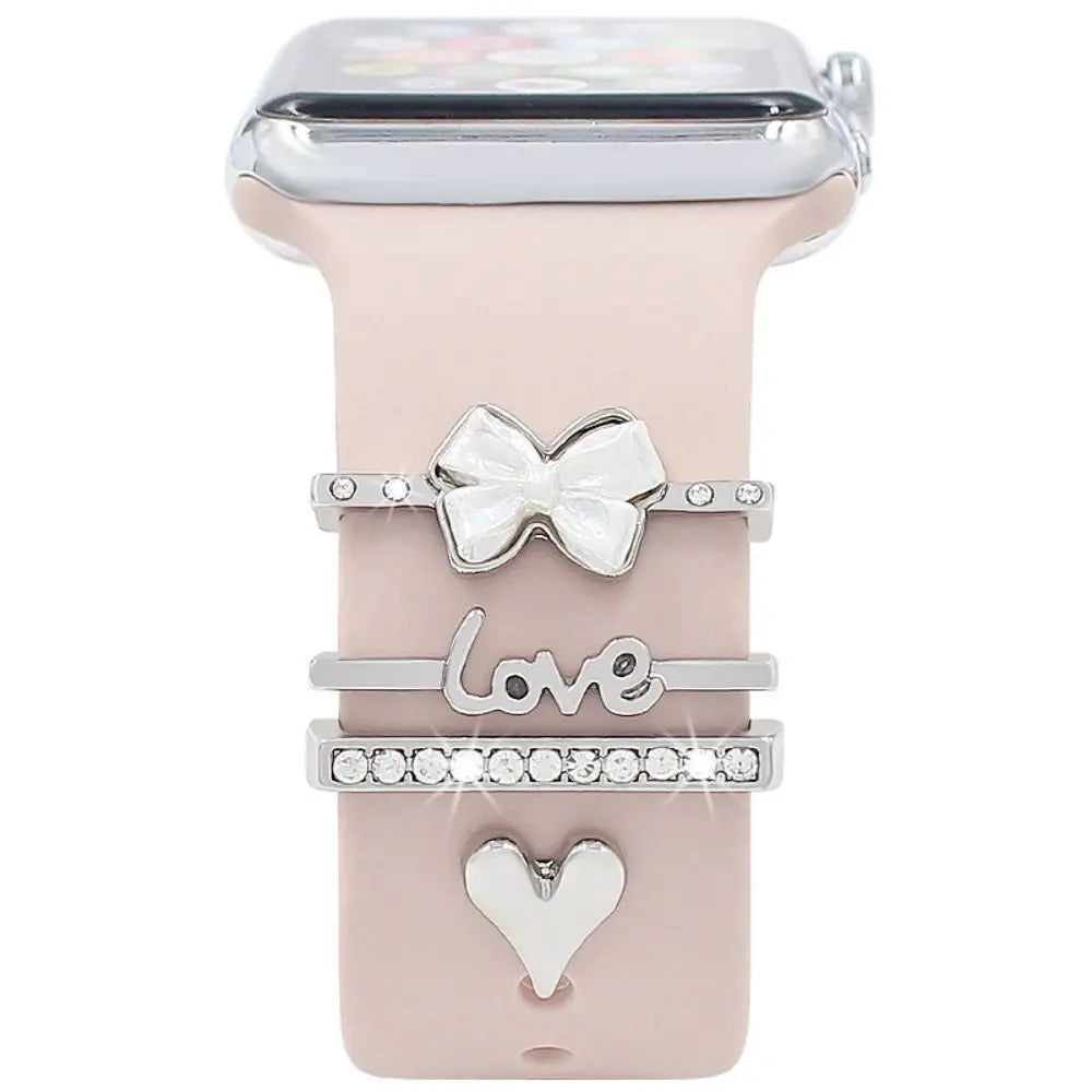 Decorative metal charms on a pink Apple Watch band, featuring bow, love, and heart designs for a stylish look.