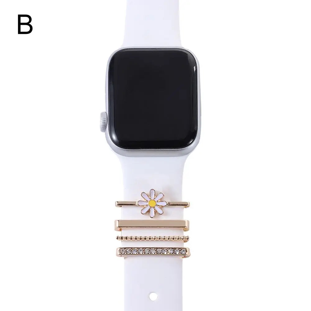 Decorative metal charms on a white Apple Watch band, featuring a flower design and gold accents for elegant smartwatch styling.
