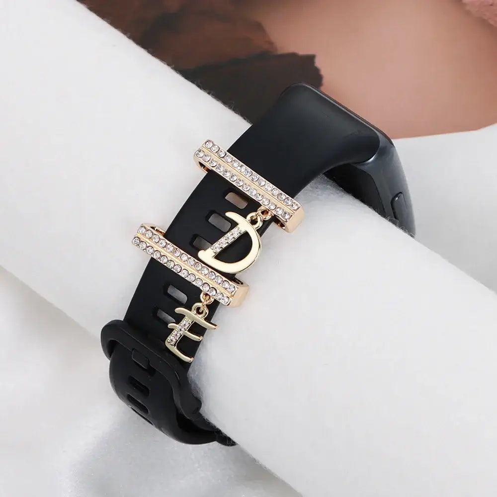 Decorative letter charms on a stylish black Apple Watch band, featuring elegant gold accents and rhinestones.