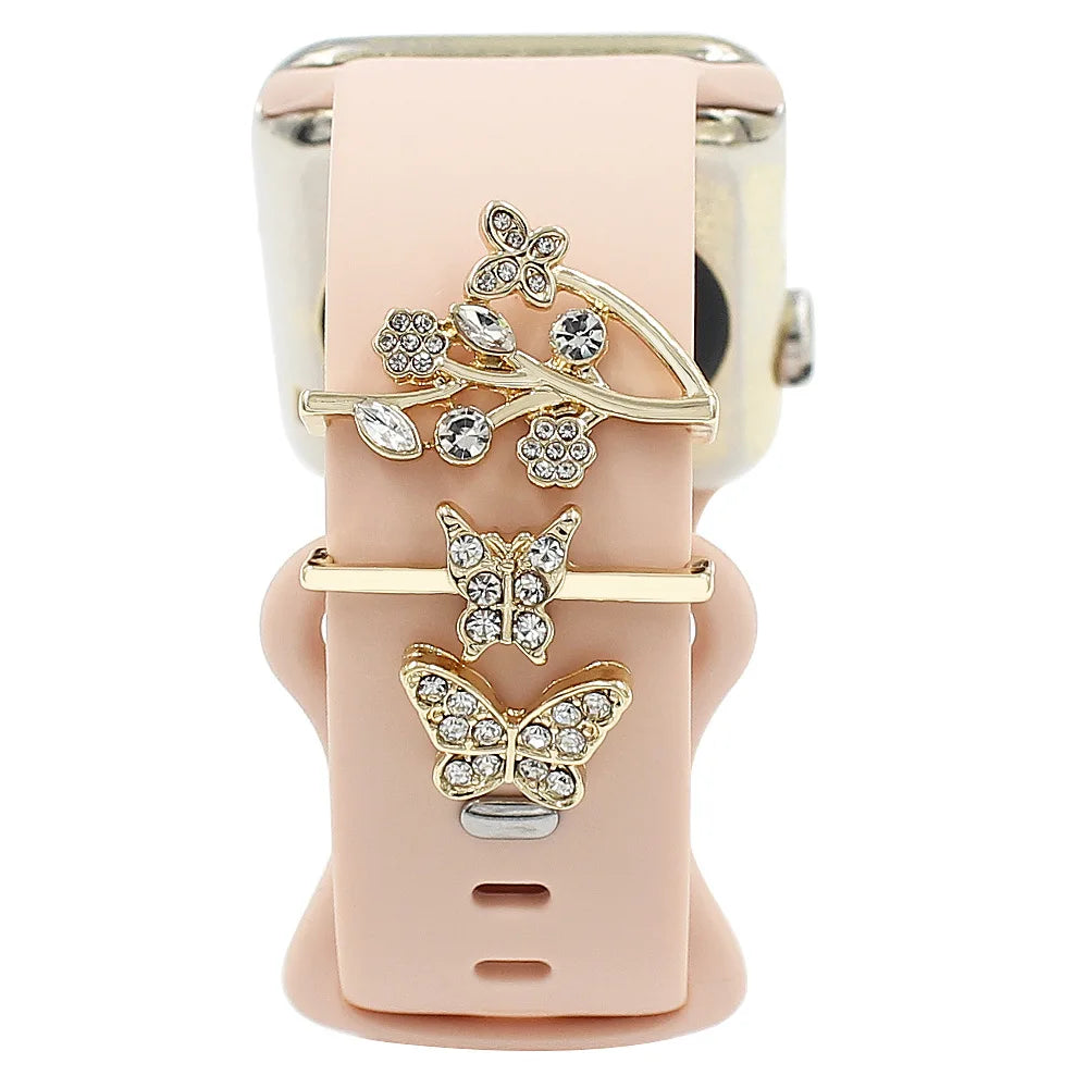 Decorative metal charms on a pink Apple Watch band, featuring butterfly designs and elegant embellishments.