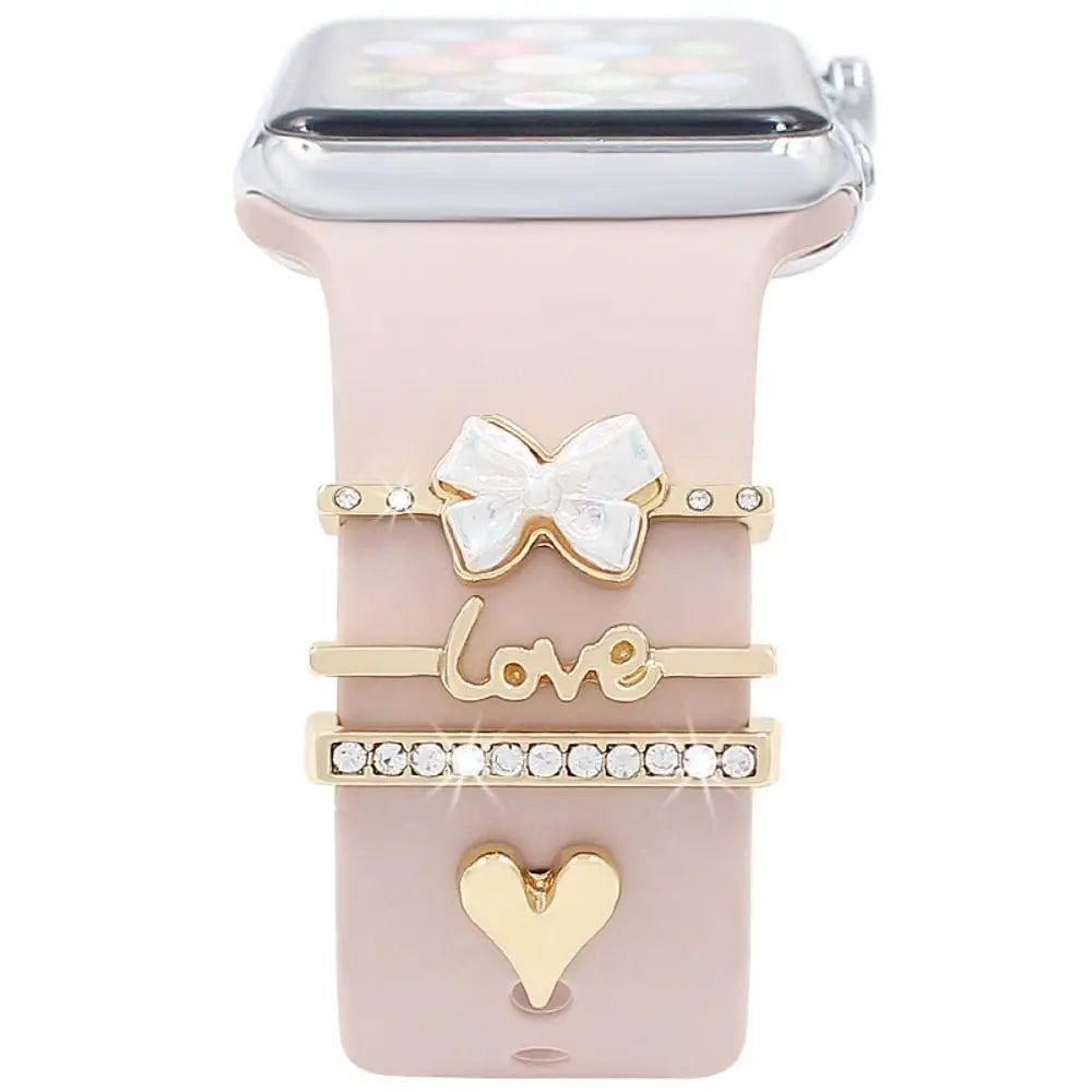Decorative metal charms on a stylish Apple Watch band, featuring 'love', bow, and heart designs for a personalized look.