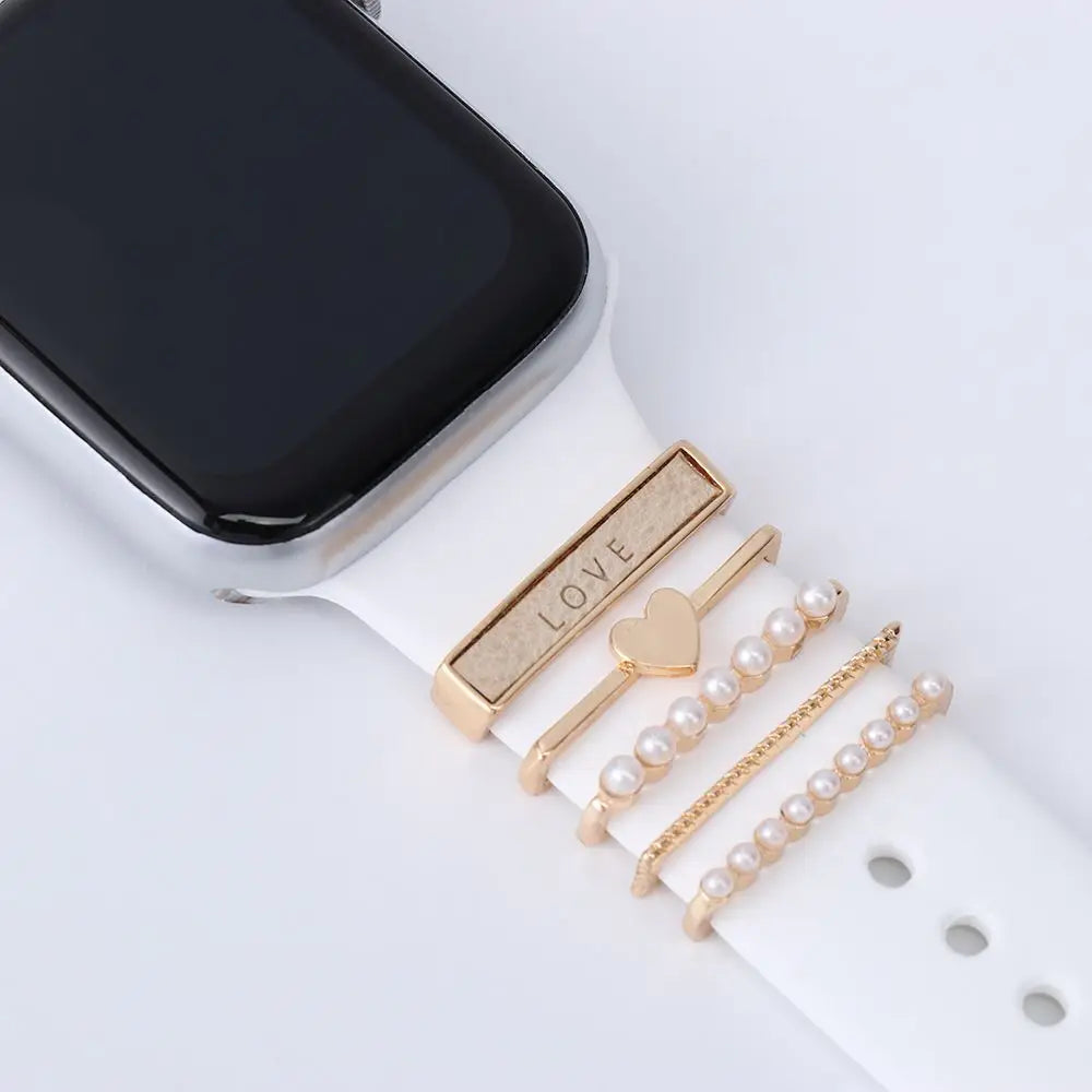 Decorative metal charms on a white Apple Watch band, featuring 'LOVE' and pearl accents for stylish elegance.