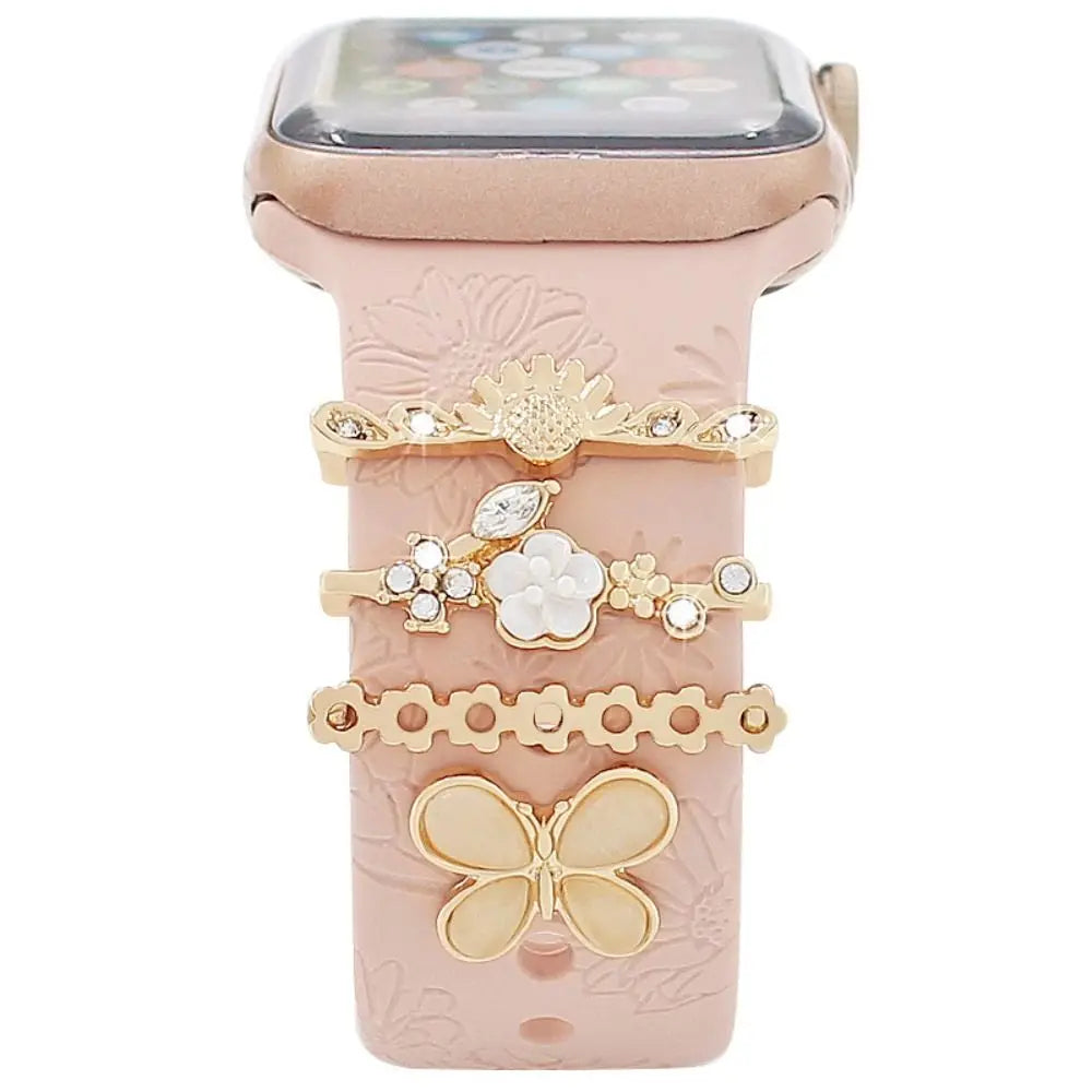 Decorative metal charms on a pink Apple Watch band, featuring floral and butterfly designs for a stylish look.