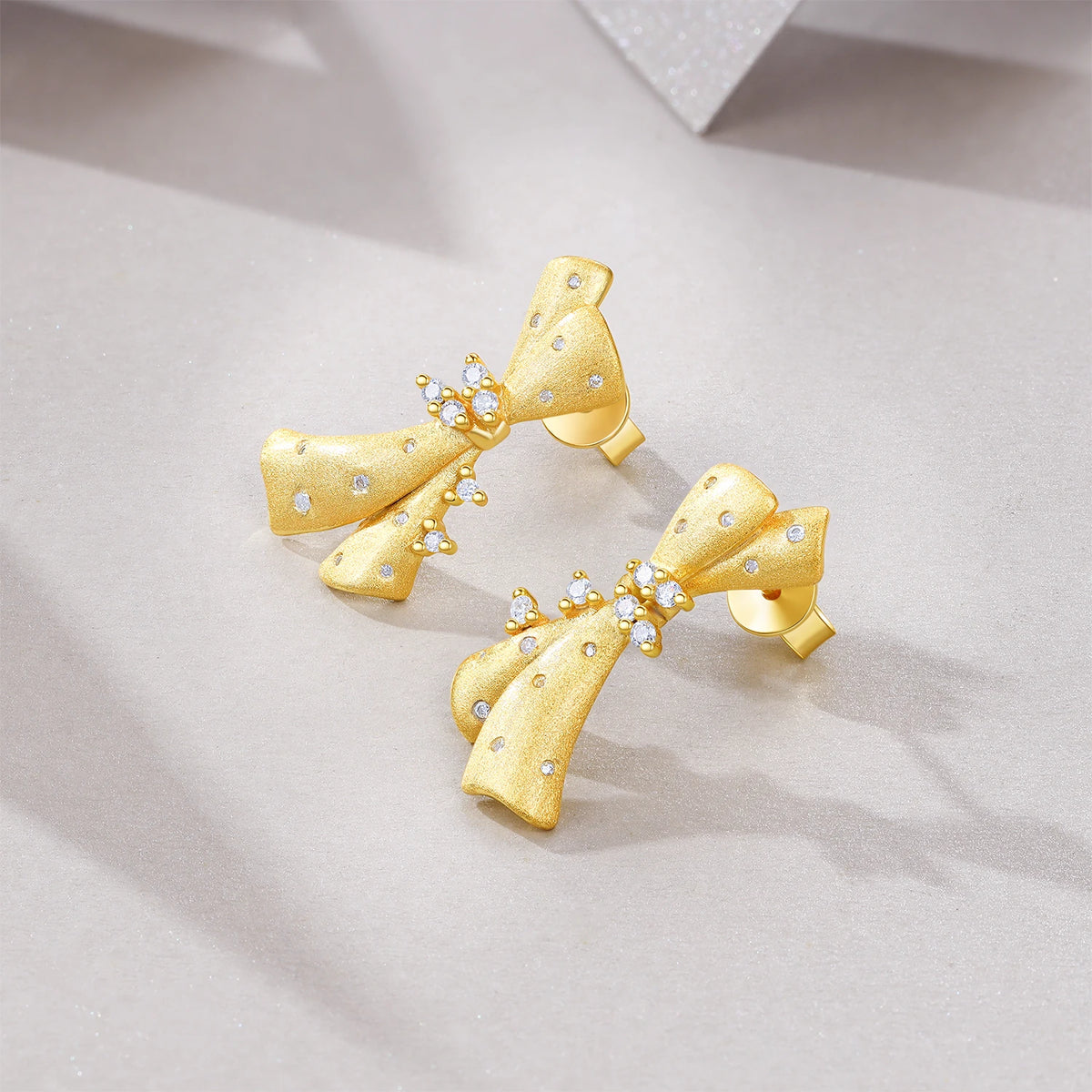 Gold-Plated Moissanite Ribbon Bow Stud Earrings — Gold bow earrings angled view — BandsCo Straps