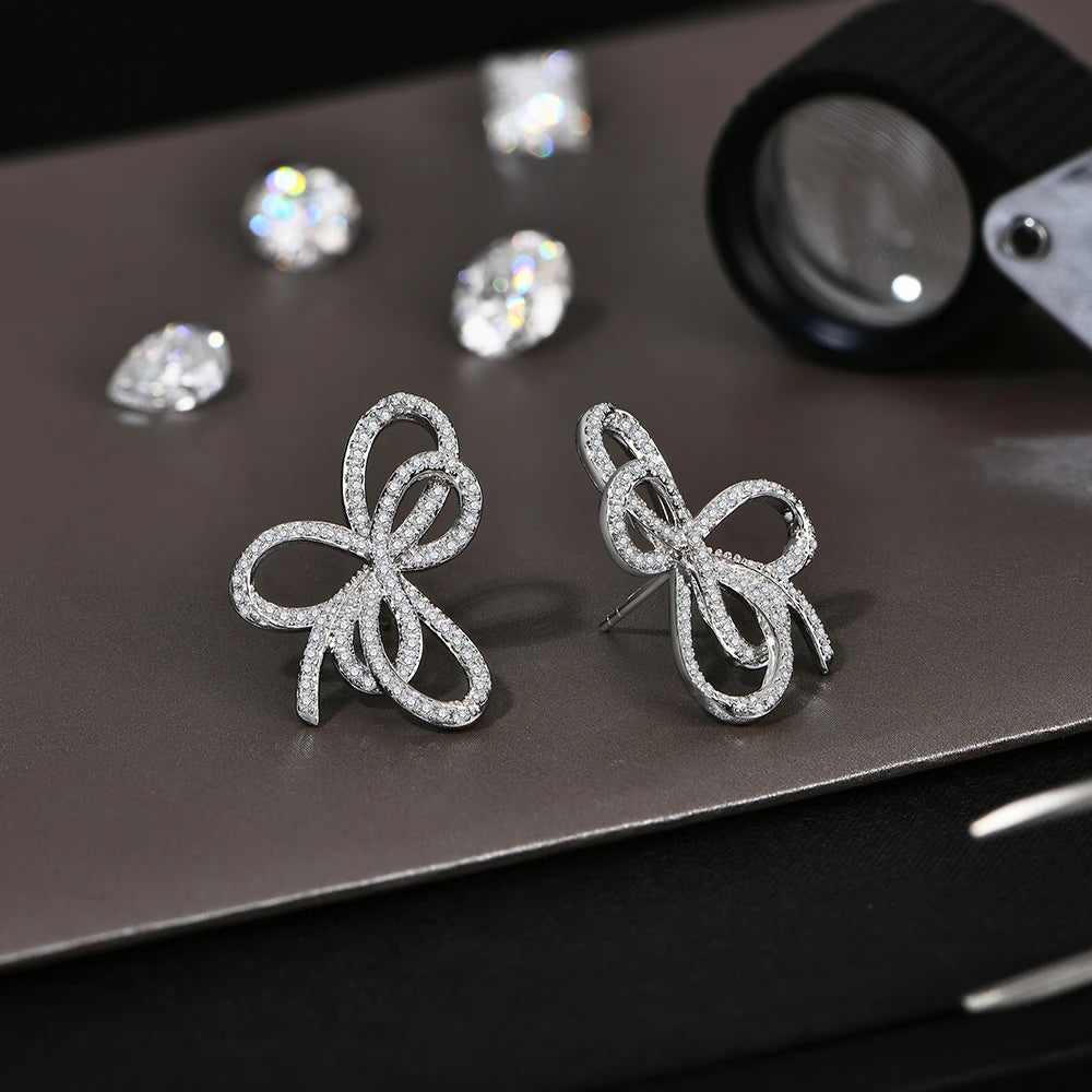 Open Bow Moissanite Stud Earrings in 925 Sterling Silver — Silver bows on dark surface